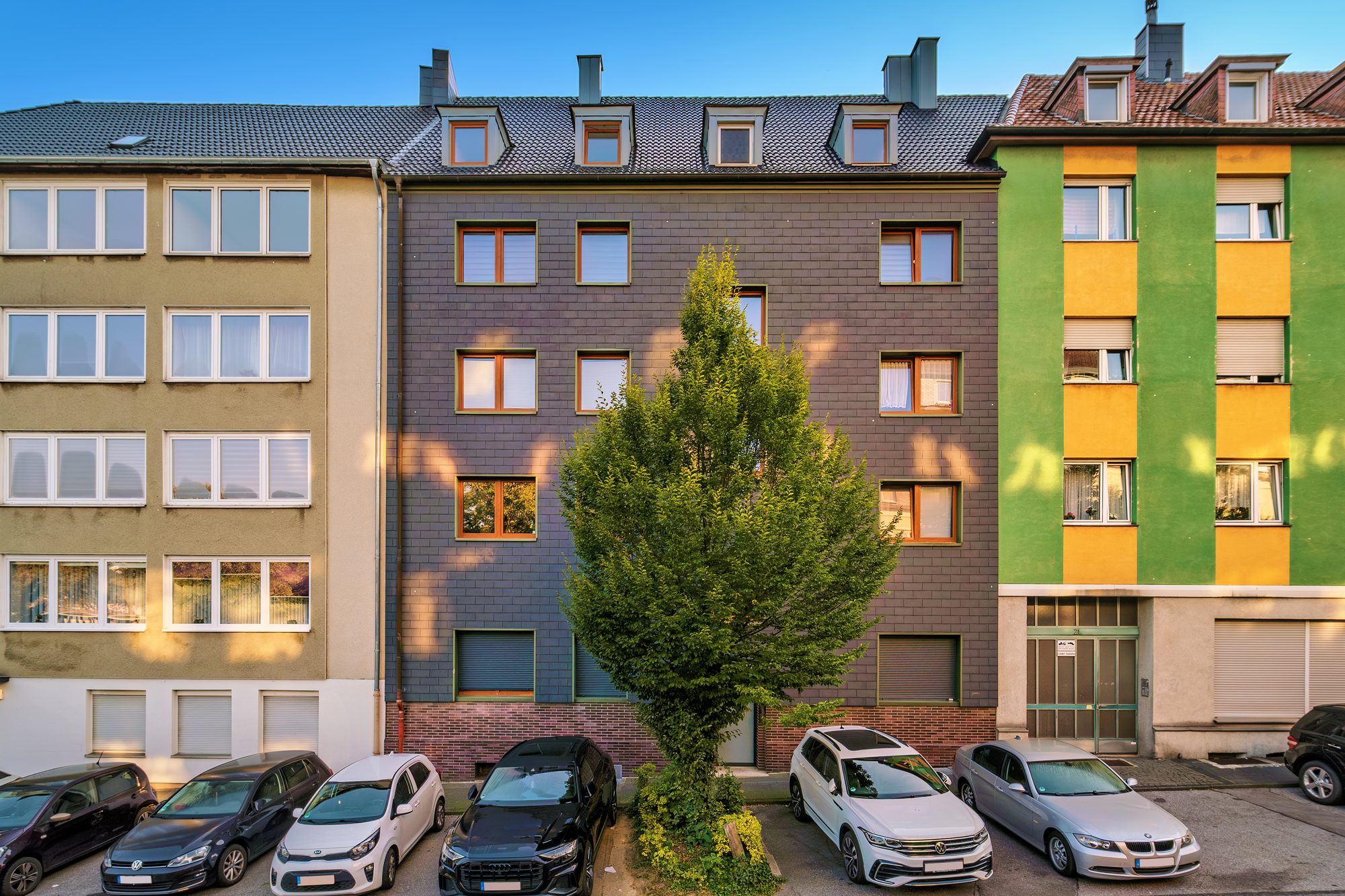 Mehrfamilienhaus mit dunkler Klinkerfassade und Mansarddach in der Häuserzeile