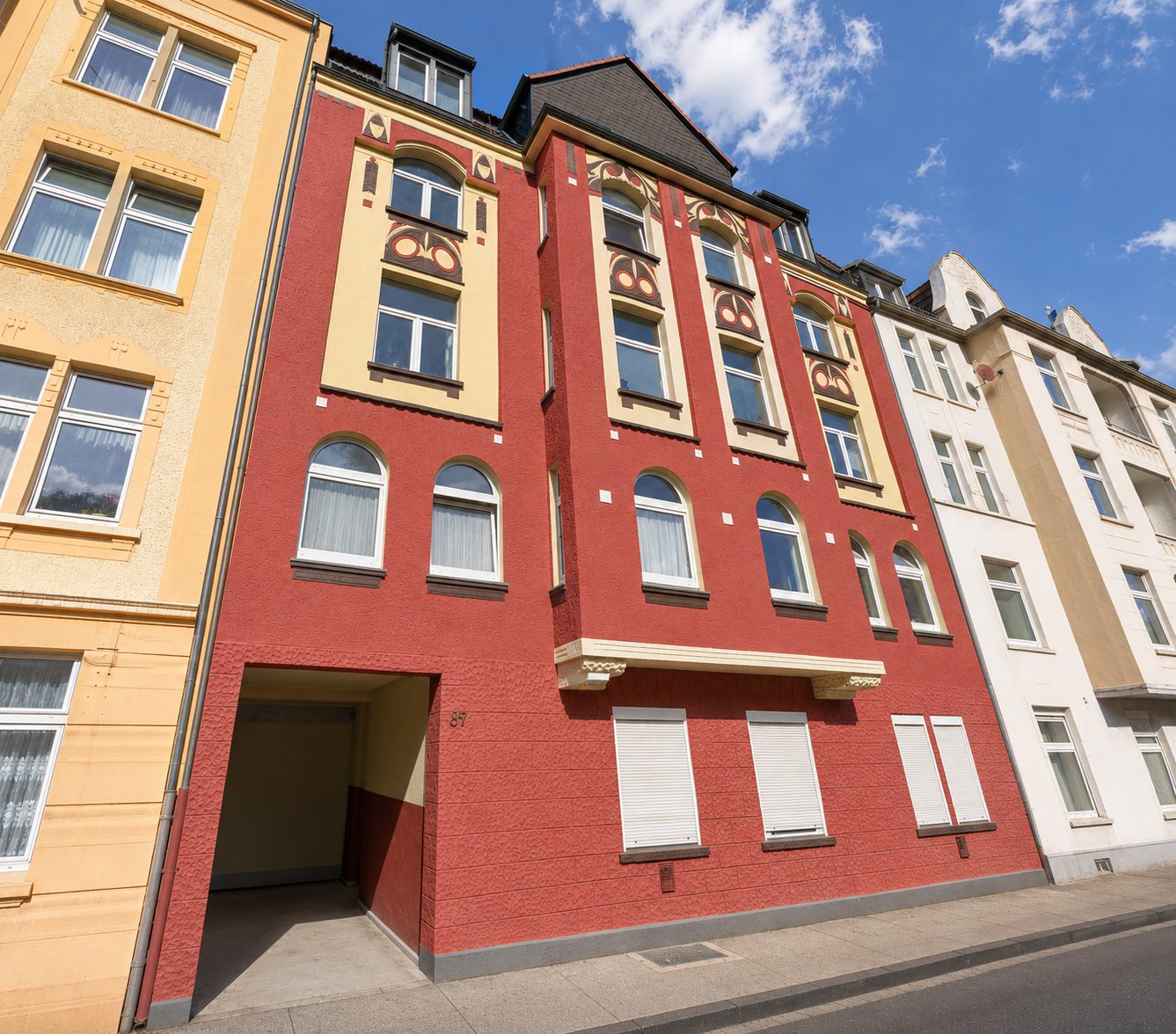 Rotes Jugendstil-Mehrfamilienhaus mit Rundbogenfenstern und Stuckdekor